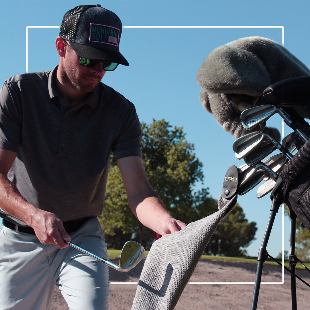 Man in gray polo and black cap cleaning golf clubs in a stylish golf bag on a sunny day.