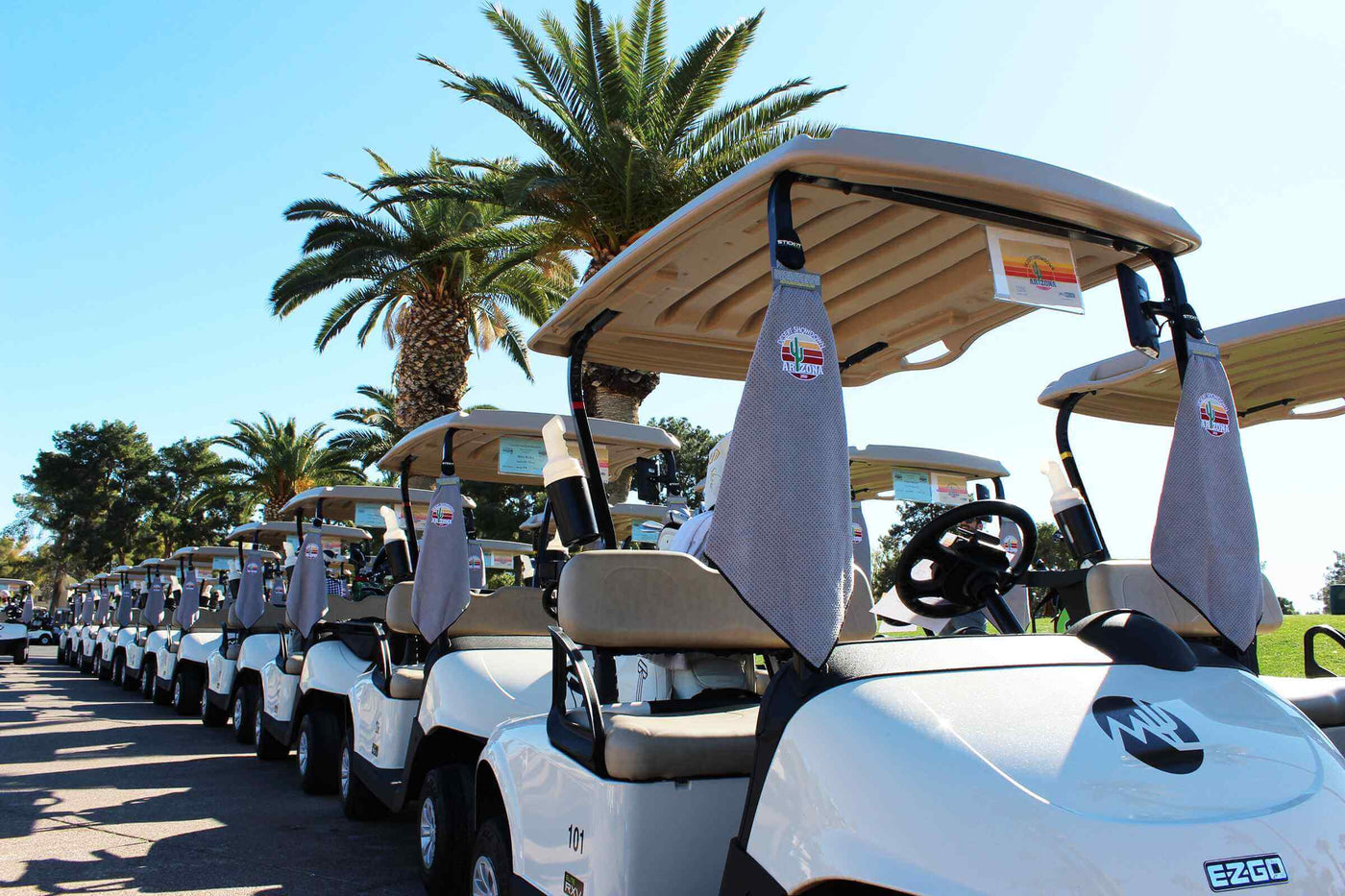 White electric golf carts lined up under palm trees, featuring beige seats and stylish grey seat covers.