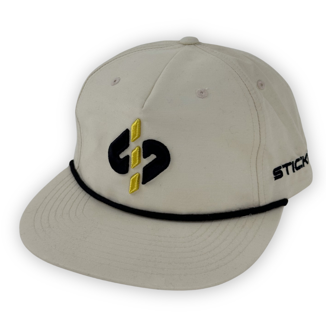 Beige baseball cap with black and yellow embroidered logo, featuring a stylish black cord around the brim.