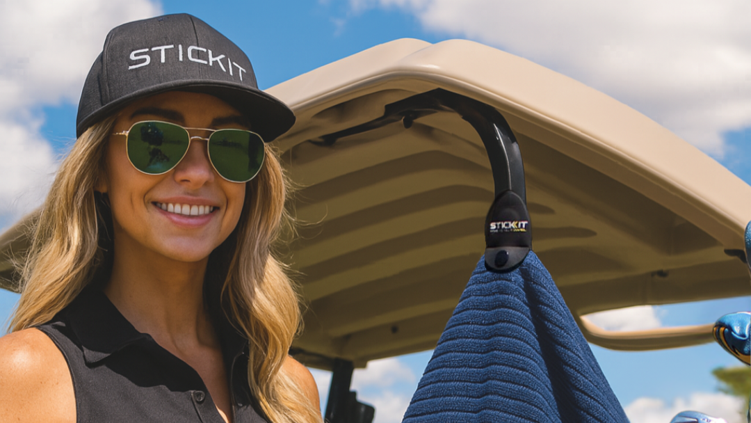 Woman in golf attire with a 'STICKIT' branded towel and cap, standing next to a golf cart.